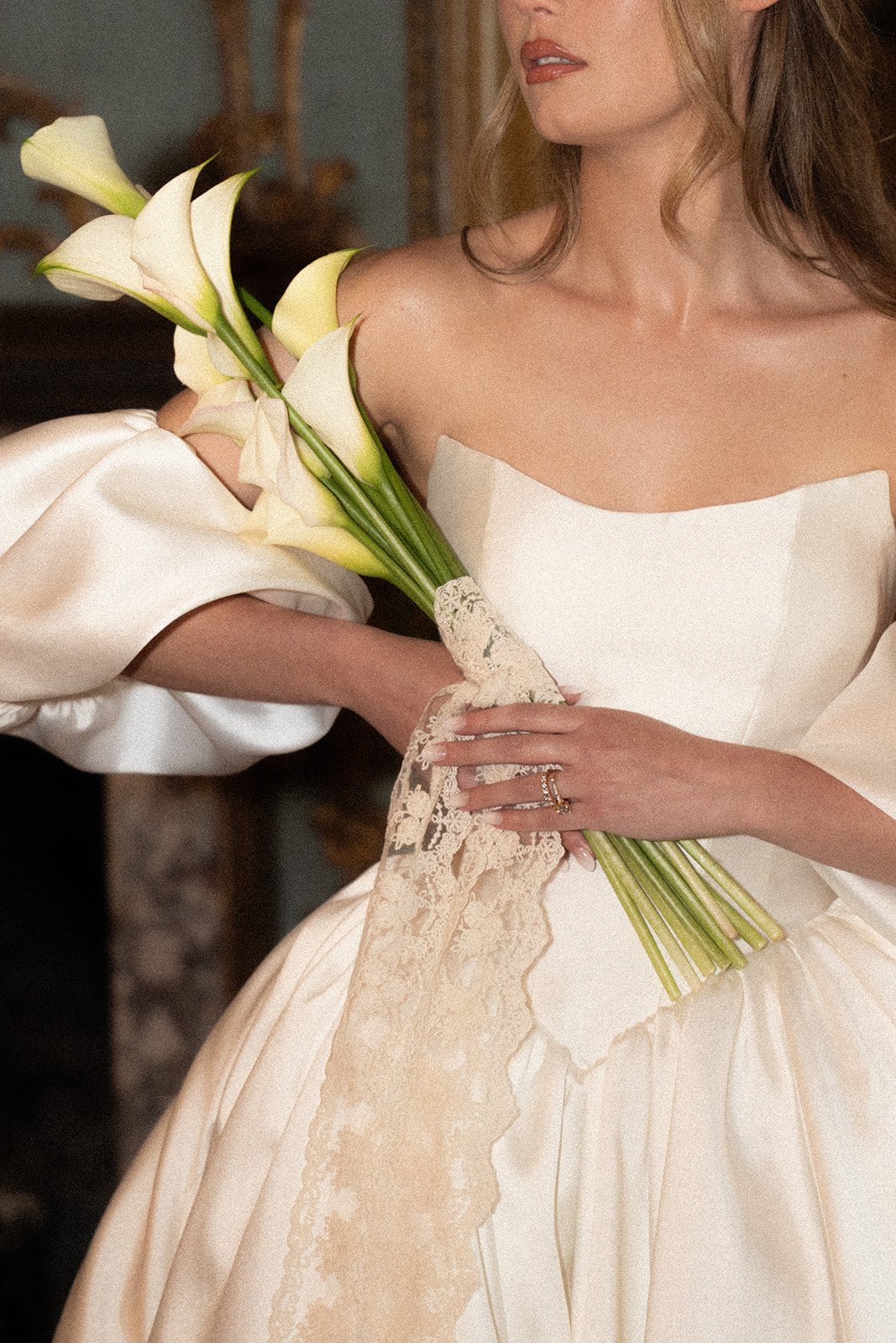 A woman in a wedding dress holding a bouquet of white calla lilies, with a lace cloth draped over her hand.